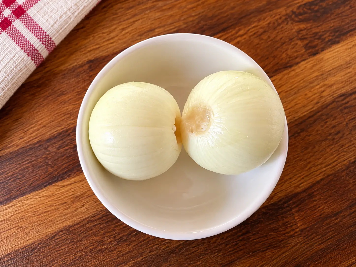 Cebolas para o Arroz com Carne de Porco Duas cebolas brancas descascadas dentro de uma tigela sobre bancada escura.